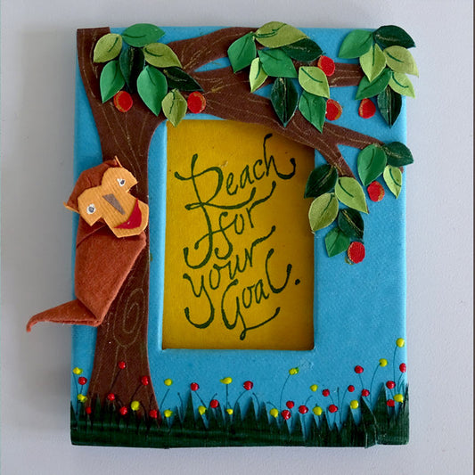 A Fridge Magnet with an origami Monkey on a paper cut-out fruit tree & the motivational quote inscribed in a window in the center of the frame.