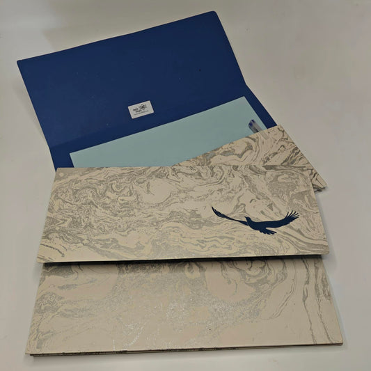 A set of decorative paper sheets and a blue folder or envelope on a plain light background. The sheets have a beige and gray marbled pattern with a dark blue bird silhouette, and one sheet is light blue.