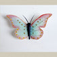 Single butterfly with open wings in blue  and shaded in the border with pink. Wings have dotted designs in yellow and maroon. Hand quilled body in dark blue colour.