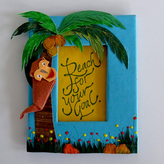 A Fridge Magnet with an origami Monkey on a paper cut-out coconut tree & the motivational quote inscribed in a window in the center of the frame.