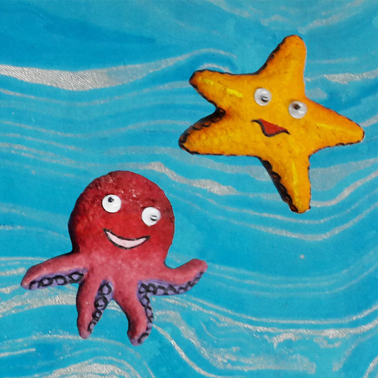 Handmade paper pulp fridge magnets shaped like an orange starfish and a red octopus, placed on a blue surface.